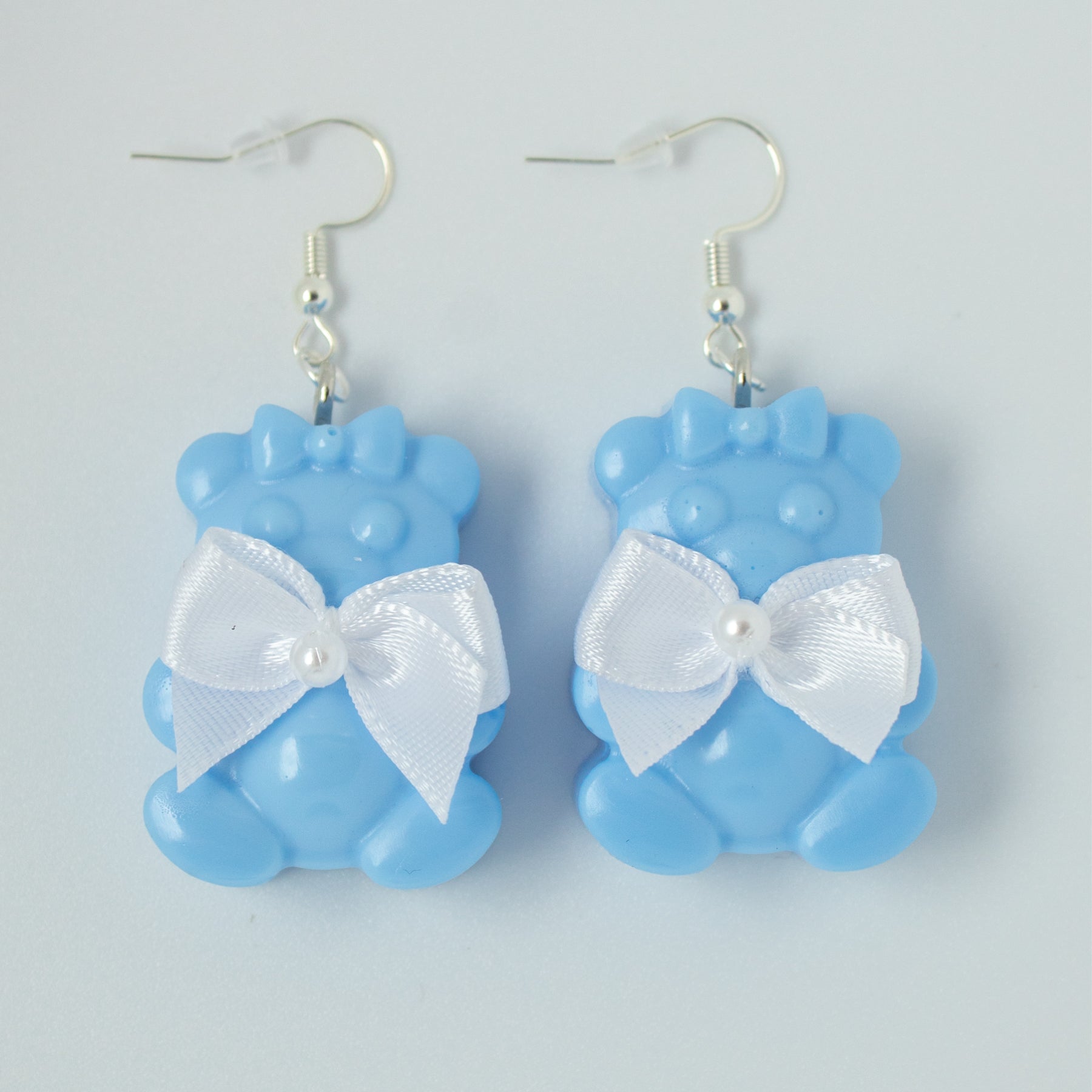 Blue bear-shaped earrings with white bows on a light gray background