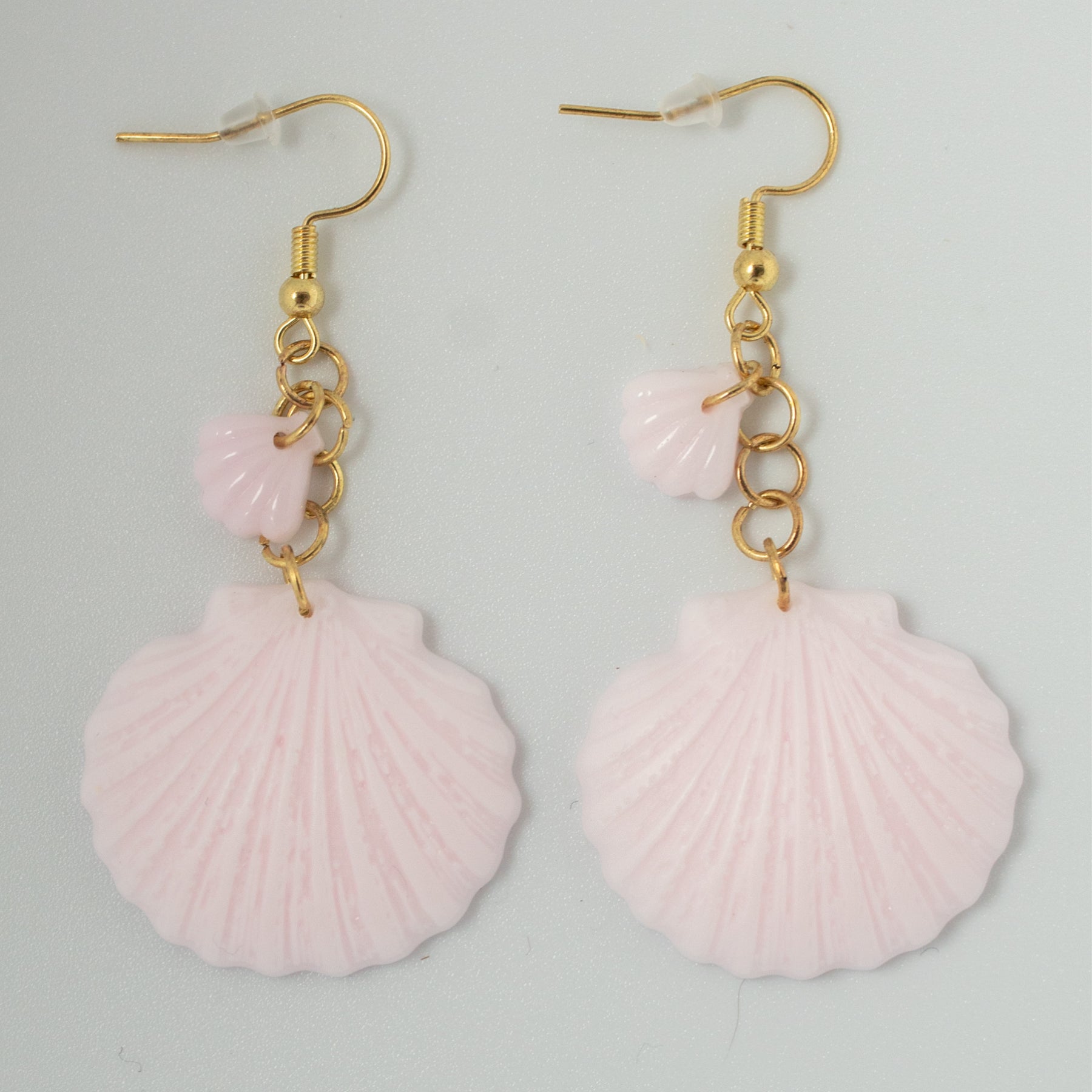 Soft pink clamshell earrings made from resin with layered detail. Lightweight, beach-inspired handmade jewelry perfect for coastal and pastel styles.