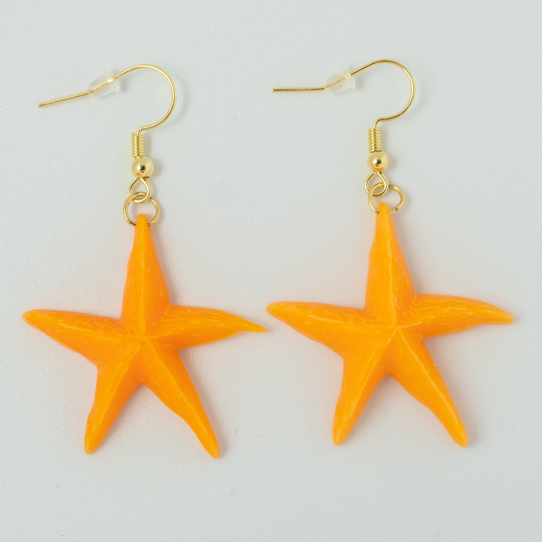 Handmade resin starfish earrings in bright orange with gold hooks on white background