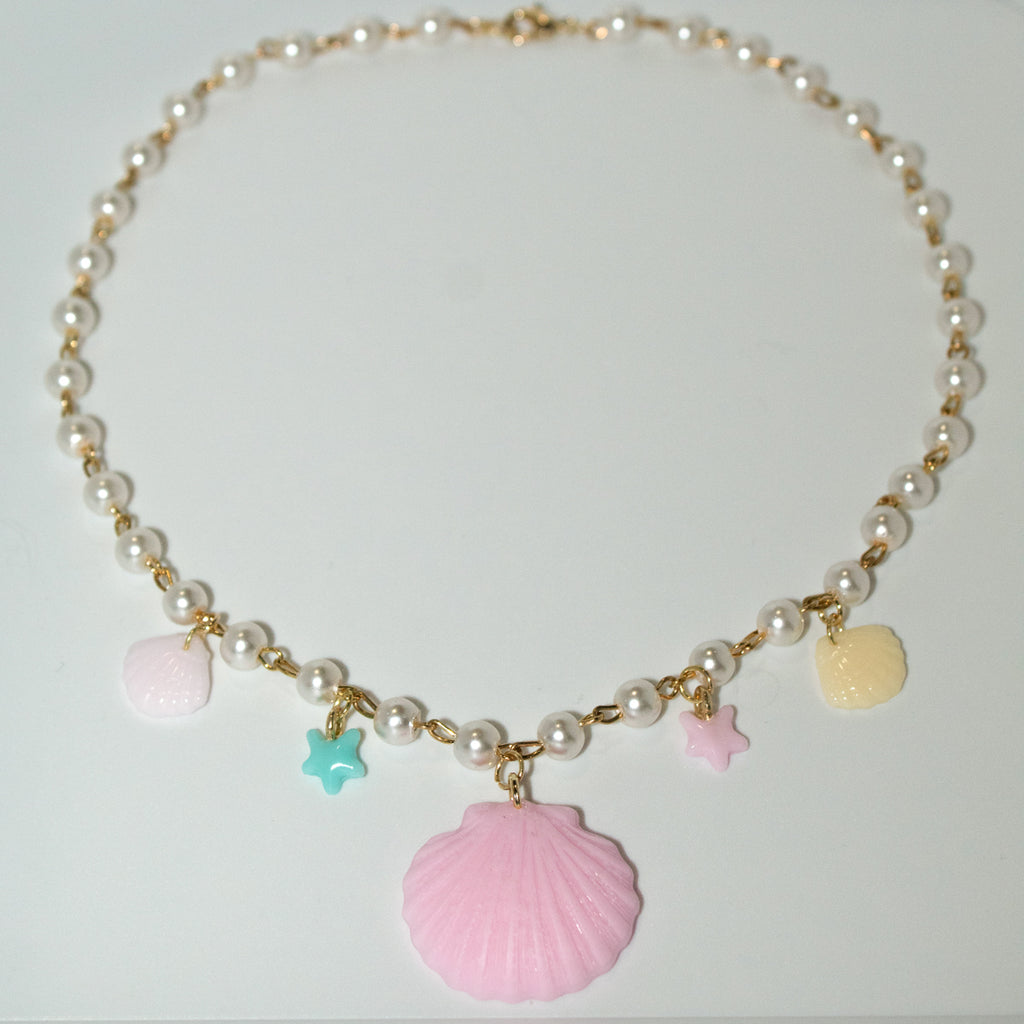 Pastel resin clamshell necklace with starfish and shell charms. Gold and pearl chain adds a dreamy, beachy touch—perfect for ocean lovers.