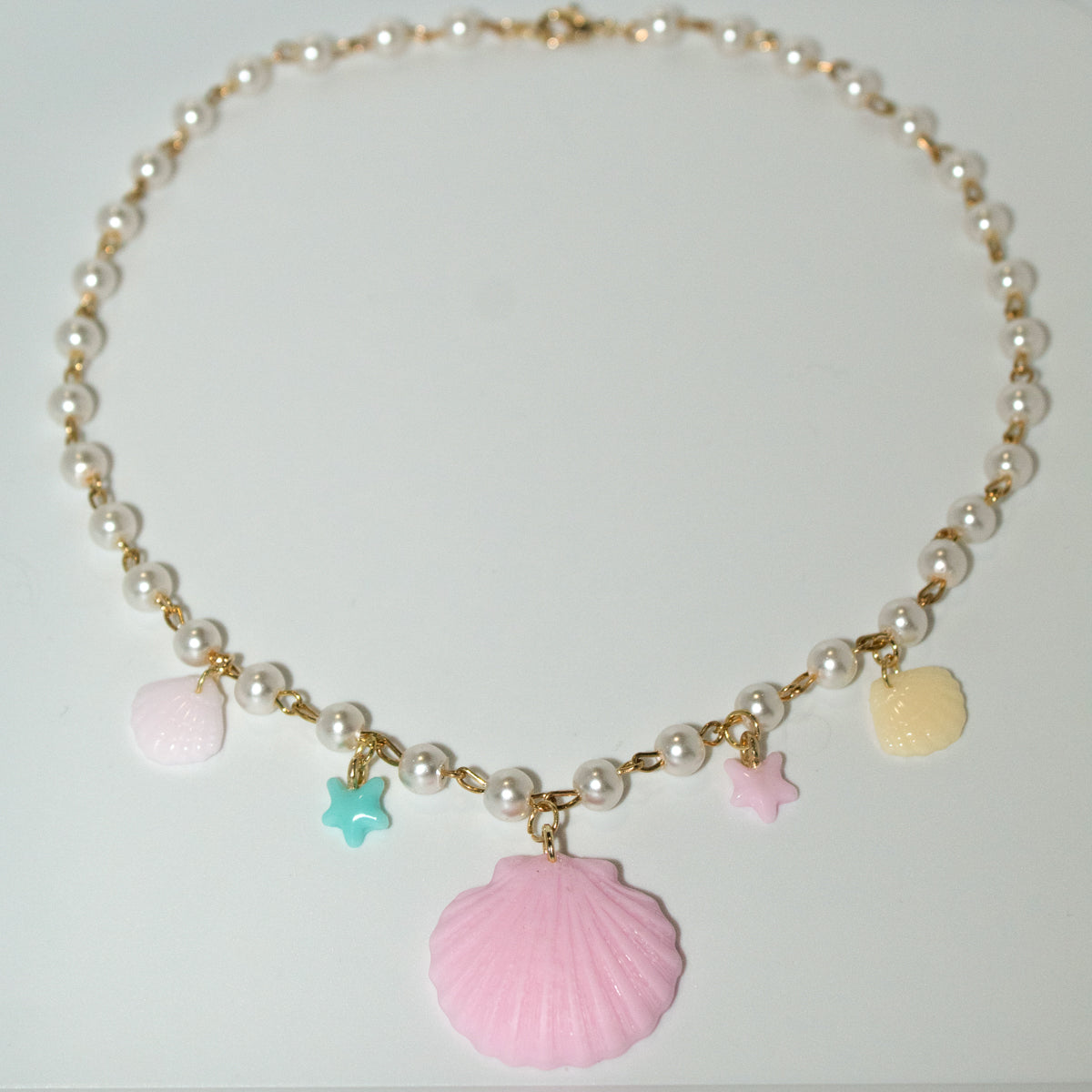 Pastel resin clamshell necklace with starfish and shell charms. Gold and pearl chain adds a dreamy, beachy touch—perfect for ocean lovers.