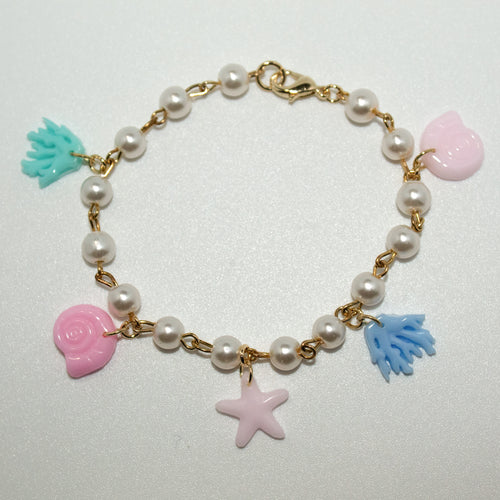 Pastel resin bracelet with coral, shell, and starfish charms on a pearl and gold chain. A dreamy ocean-themed accessory for beach lovers.