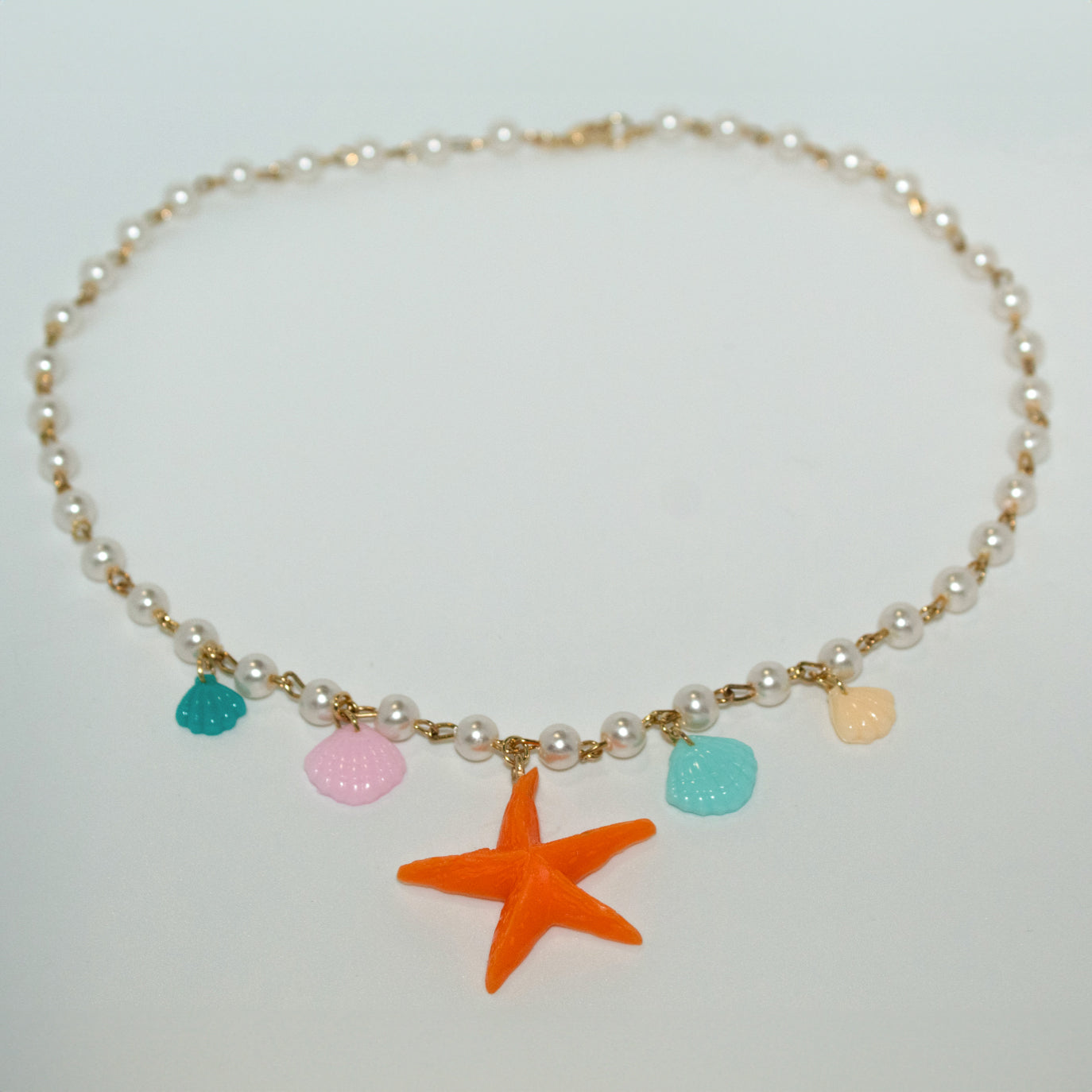 Vibrant orange starfish necklace with pastel shell charms on a pearl and gold chain. Beachy, playful, and perfect for summer or mermaidcore outfits.