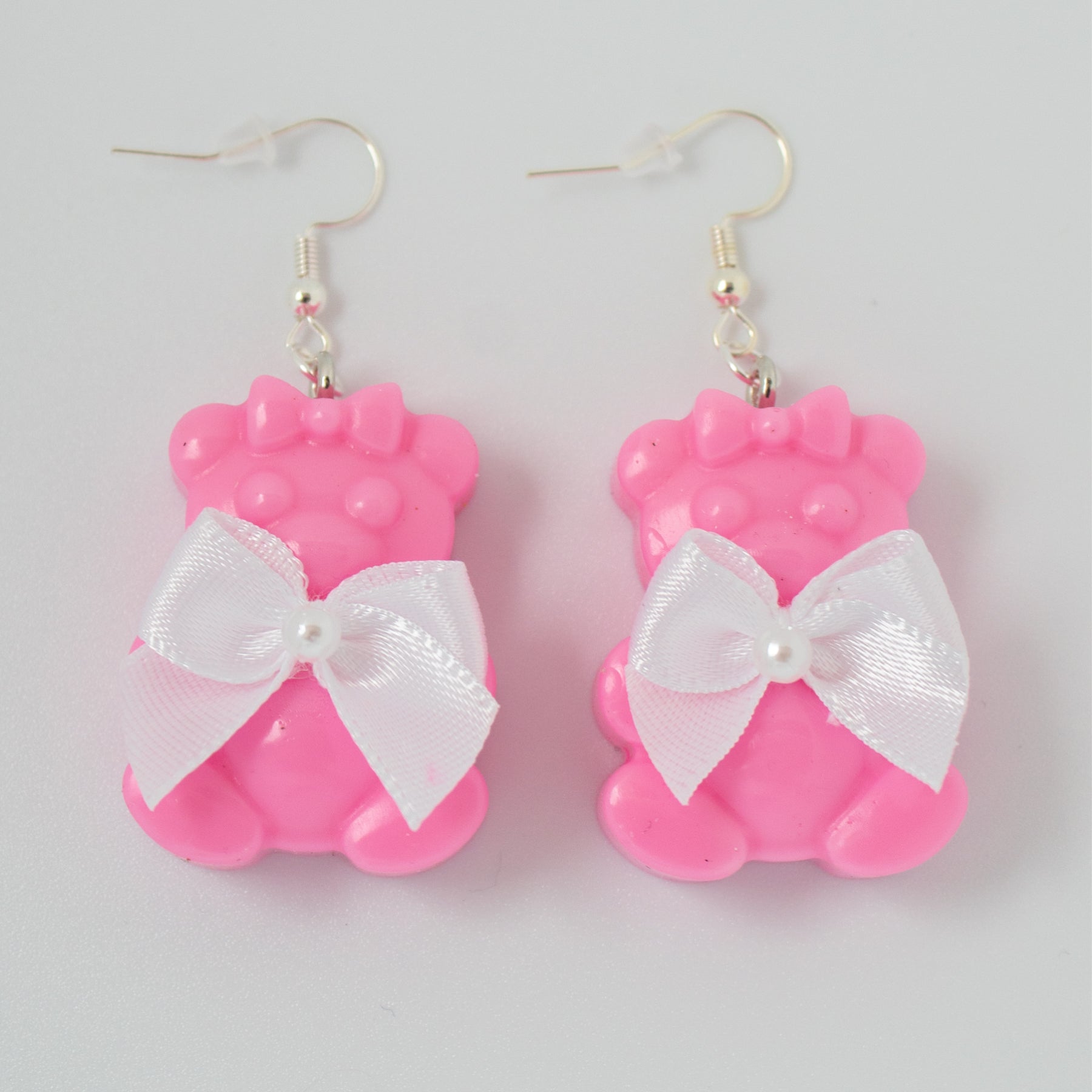 Pink bear-shaped earrings with white bows on a light gray background