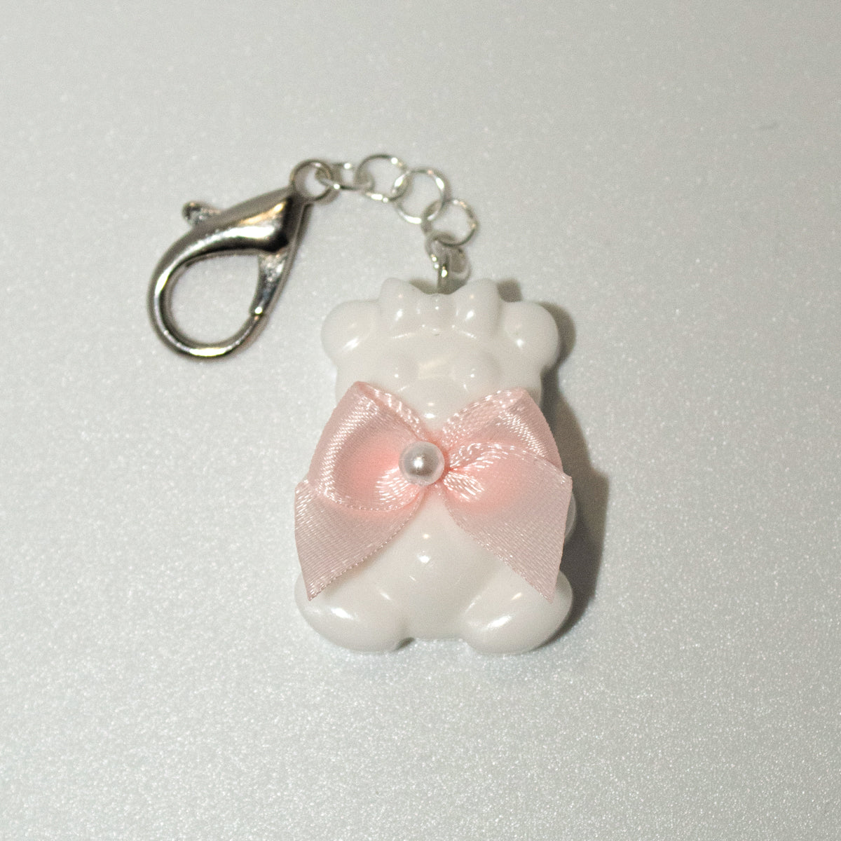 White bear-shaped keychain with a pink bow on a light gray background