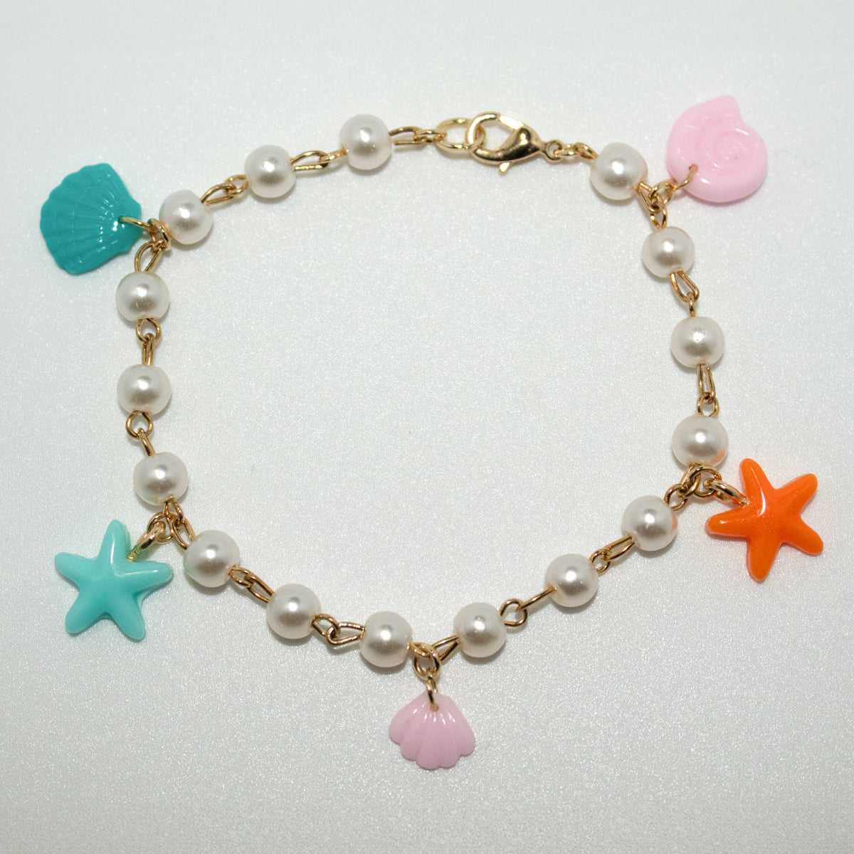 Ocean charm bracelet with resin starfish, clamshells, and swirl shell on a pearl and gold chain. Playful and perfect for beach lovers or mermaidcore style.