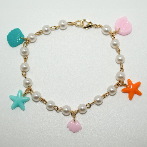 Ocean charm bracelet with resin starfish, clamshells, and swirl shell on a pearl and gold chain. Playful and perfect for beach lovers or mermaidcore style.