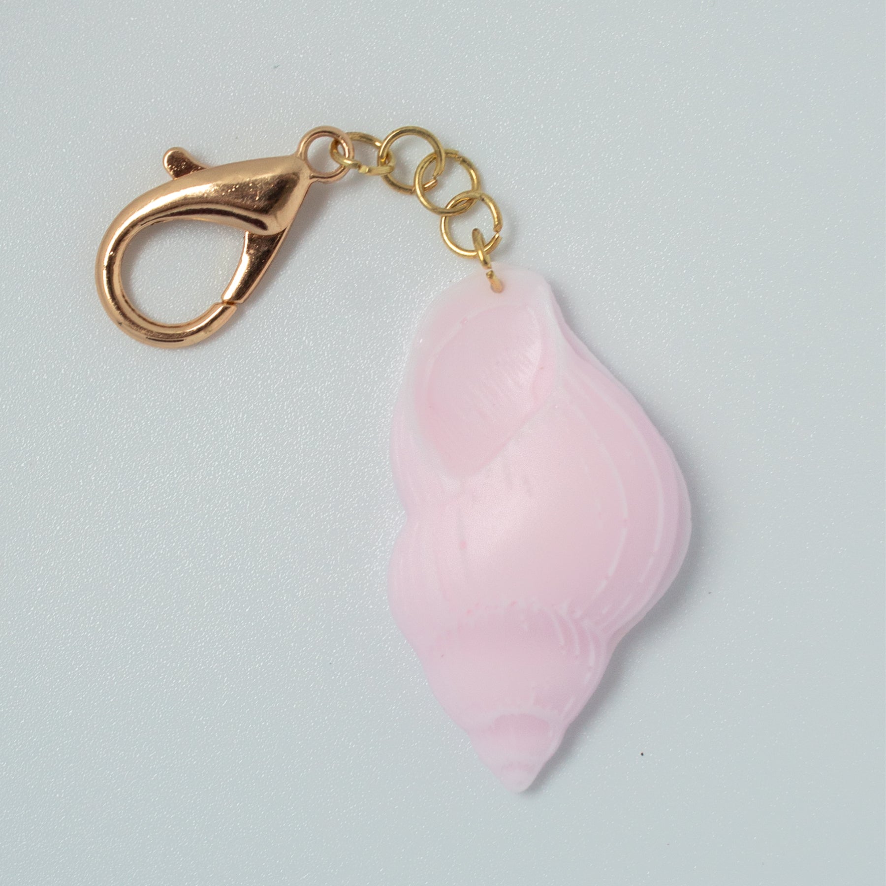 Close-up of light pink spiral shell resin keychain with gold clasp.